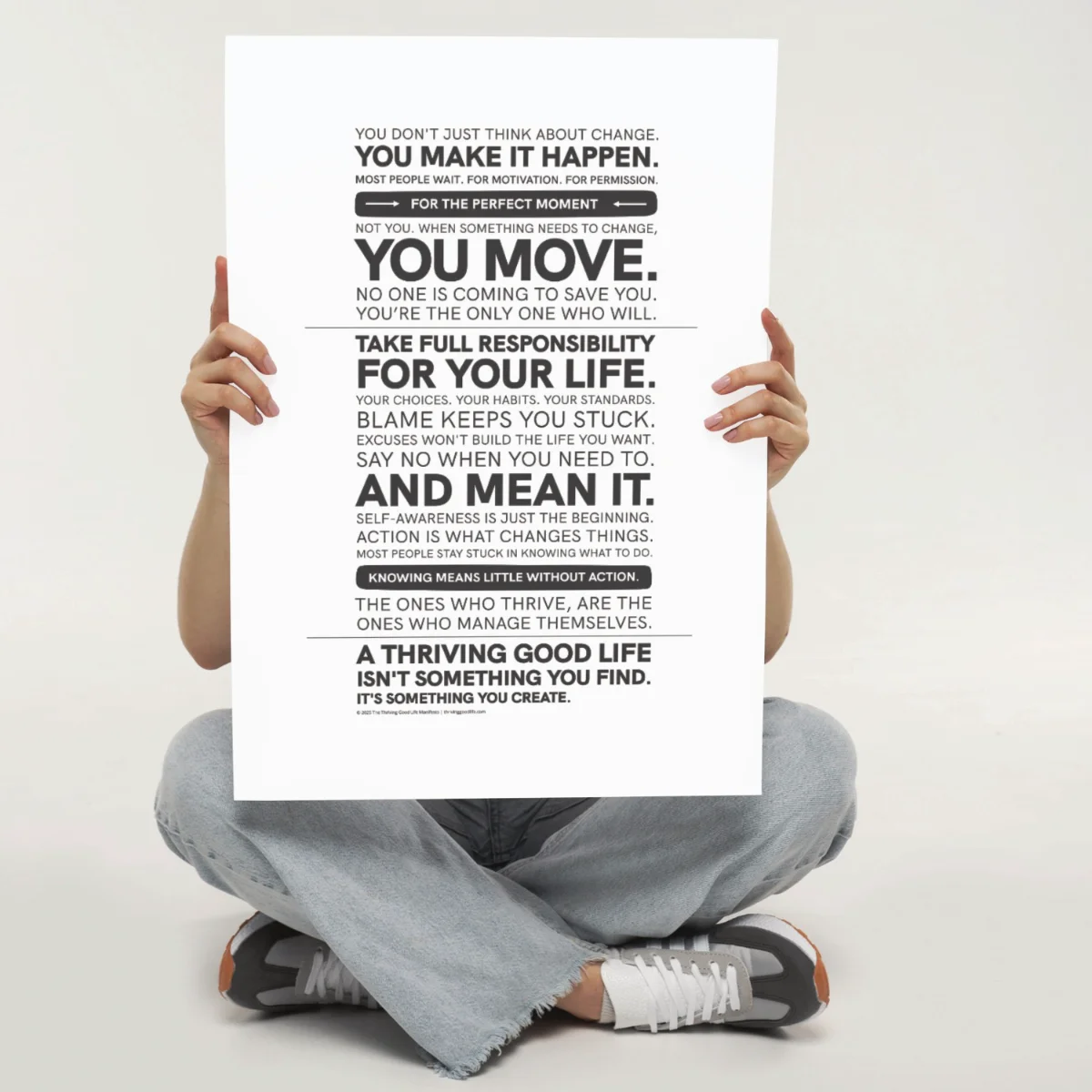 Person sitting cross legged holding the Thriving Good Life Manifesto Poster — bold black-and-white motivational wall art about self-management and accountability.